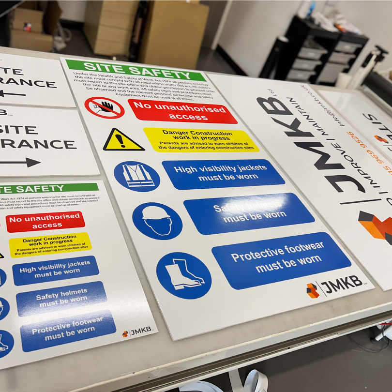 The image shows a collection of site safety signs branded for local construction company JMKB