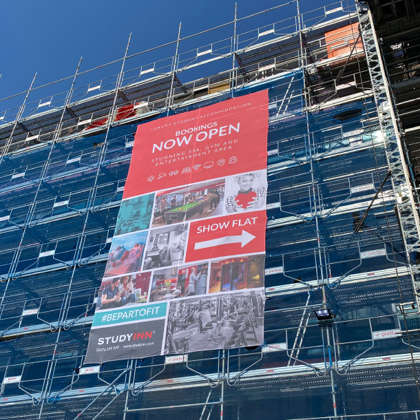 The image shows scaffold on a large tall building with blue netting around it. Over the blue netting is a large printed banner advertising 'Study Inn' the student accomodation being built.